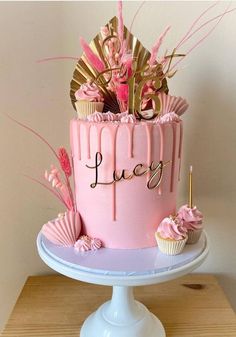 a pink and gold birthday cake with cupcakes on the side that says juicy