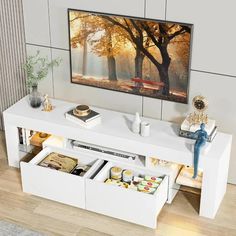 a white entertainment center with drawers underneath a painting on the wall and a television in the background