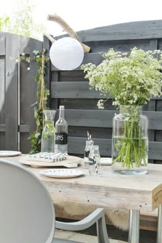 a wooden table topped with vases filled with flowers next to a white plate and silver chairs