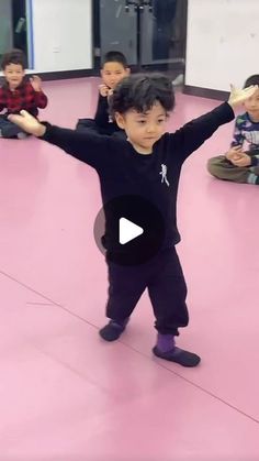 a little boy standing on top of a pink floor in front of other children sitting down