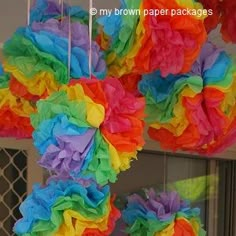 multicolored tissue pom poms hanging from the ceiling in front of a window