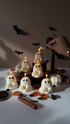 a person lighting candles in front of small white ghost heads and bats on a table