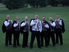 a group of men standing next to each other on a lush green golf field with trees in the background