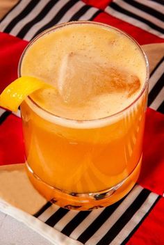 an orange drink with a slice of lemon on the rim sits on a red and black checkered tablecloth