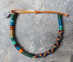 an orange, blue and green beaded bracelet with a silver charm on a rock