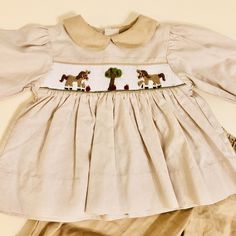 This is a precious ham, smocked two piece outfit. Dress style top in tan and white tiny gingham check. Baby wale corduroy peter pan collar and wrists. Buttons in back with buttons at wrists. Missing bottom button, shown in last image. Hands smocked with horse/ponies, apples and apple tree. Tan baby wale corduroy elastic waist pull on pants with elastic ruffle at leg. New with tags condition. Hard to find outfit. Brand - Petit Ami Size reads- 6 months Measurements – top – 12 inches long, 10 inche Horse Pony, Hand Smock, Luxury Lifestyle Dreams, Outfit Dress, Gingham Check, Baby & Toddler Clothing, Pan Collar, Peter Pan Collar, Pull On Pants