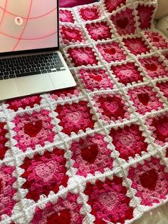 a laptop computer sitting on top of a pink and white crocheted blanket next to a bed