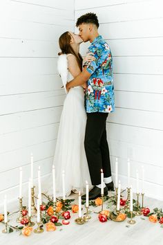 a bride and groom kissing in front of candles on the floor with flowers all around them