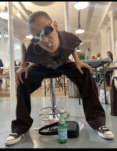 a young man sitting on top of a stool next to a bottle of beer and sunglasses