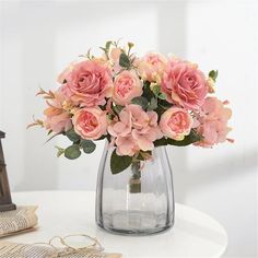 a vase filled with pink flowers sitting on top of a table next to a book