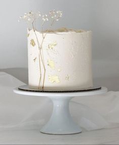 a white cake with gold leaf decoration on top is sitting on a plate and it's ready to be cut