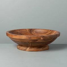 a wooden bowl sitting on top of a table next to a gray wall and floor