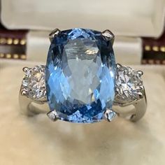 an oval blue and white diamond ring with three diamonds on the side, in front of a box