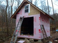 a house being built in the woods with ladders on it's sides and windows