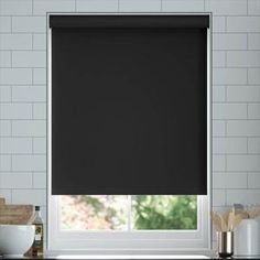 a black roller shade in a kitchen window with white subway tiles on the wall behind it