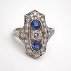 Art Deco 14k (.585) white gold long ring, decorated with Diamonds and Sapphire stones. There are 22 single cut Diamonds, approx. 1.55 mm, the center stone is Old Mine Cut 4.67 x 4.2 x 3.25 mm, color K, SI1 clarity. 2 natural Sapphires are 4.27 mm in diameter. This stately ring is a size 5, it is 22 mm long, weighing 2.7 grams. EA4815 White Gold Marquise Multi-stone Diamond Ring, Diamond White Marquise Multi-stone Ring, Diamond White Multi-stone Marquise Rings, Art Deco Diamond Jewelry With Gemstone, White Gold Multi-stone Round Sapphire Ring, Multi-stone Round Sapphire Ring In Platinum, White Gold Sapphire Ring With Multi-stone, Art Deco Diamond Cluster Ring With 17 Jewels, Diamond White Marquise Multi-stone Jewelry