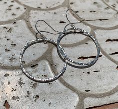 These hoop earrings are entirely hand-made of sterling silver wire. The hoops were formed by hand, soldered, and then given a bark-like texture with the edge of my favorite hammer. In the photos showing two pairs of earrings the medium size (for this listing) are the larger ones shown at the top of the photo. MEASUREMENTS These earrings each measure 2" long from the top of the hook. Each circle measures 1 & 3/8"" in diameter. Artisan made, with love, in my small home studio in Springfield, Oregon. Made by own hands from sterling silver wire, smithing tools and fire. If you have any questions about individual pieces, or my process, please feel free to ask me using the contact seller button. I'm happy to answer them. If you would like to see more of my silver work please visit my shop here: Silver Circle Earrings, Hammered Sterling Silver, Silver Circle, Silver Work, Hammers, Circle Earrings, Small Home, Jewelry Earrings Hoops, Silver Wire