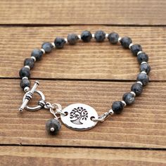 "This bracelet measures 8\" long (20cm) and fits a 6.75\" wrist. It features a silver tone link with a bird in tree design.  I have paired it with black and grey Norwegian moonstone beads (larvikite/black labradorite). The clasp, small beads, and link are made of silver plated leadfree pewter.  The jump rings are made of silver colored enameled copper and antiqued silver plated base metal.  The crimp beads, wire guardian, and crimp covers are made of sterling silver.  The headpin is made of antiqued silver plated base metal.  The bracelet is strung on Soft-Flex wire which is supple and strong. The tree component is made in the US.  It measures 3/4\" long (19mm). ---------------------------- Thank you for browsing my shop! If you'd like to see my necklaces and jewelry sets, click here: http Adjustable Gray Metal Jewelry, Adjustable Gray Jewelry With 8mm Beads, Bohemian Silver Charm Bracelet With 8mm Beads, Silver Bohemian Charm Bracelet With 8mm Beads, Adjustable Silver Rosary Bracelet With Gemstone Beads, Adjustable Gray Sterling Silver Jewelry, Spiritual Gray Bracelet Jewelry, Silver Charm Bracelet With Gemstone Beads, Silver Labradorite Gemstone Bead Bracelets