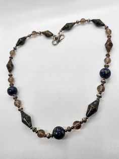 Apache pyrite, lapis lazuli and smoky quartz beaded sterling silver artisan necklace. The beads on this unique necklace are one of a kind. Each gemstone bead is unique in the pyrite inclusions that are found through out the stones. The Apache pyrite elongated bicone beads are full of amazing color and heavy. The lapis lazuli is mottled with a large amount of shining gold highlights through the blue lapis. There are sterling silver and smoky quartz beaded spacers between. Stamped 925 on the hook Unique Silver Beaded Necklace With Faceted Beads, Artisan Silver Jewelry With Faceted Beads, Artisan Jewelry With Faceted Beads In Silver, Artisan Silver Necklaces With Faceted Beads, Silver Jewelry With Faceted Beads Made Of Lapis Lazuli, Silver Beaded Necklaces With Lapis Lazuli Natural Stones, Silver Jewelry With Faceted Beads In Lapis Lazuli, Silver Beaded Necklace With Lapis Lazuli Natural Stones, Silver Beaded Necklace With Natural Lapis Lazuli Stones