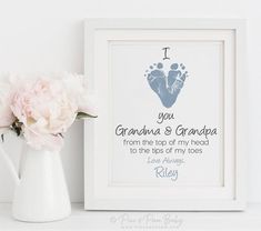 a white vase filled with pink flowers next to a framed baby's foot print