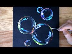 a person is drawing bubbles on a piece of black paper with colored pencils and markers