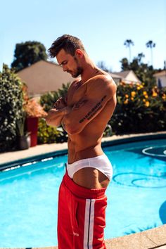 a man standing in front of a swimming pool with his shirt off and arms crossed