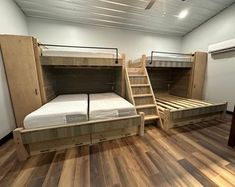 two bunk beds in a room with wooden floors and white walls, one has a ladder to the top