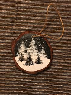 a wooden ornament hanging on a string with trees in the snow behind it