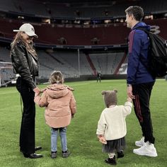 a man and woman holding hands with two small children on a field at a stadium