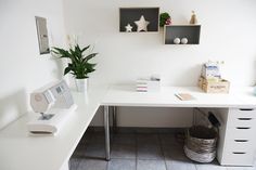 a white desk topped with a computer monitor next to a potted plant on top of a table