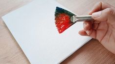 a hand holding a paintbrush painting a piece of white paper with red and green colors