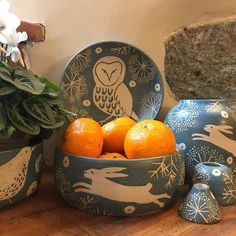 two oranges in a bowl next to an owl and other decorative items on a table