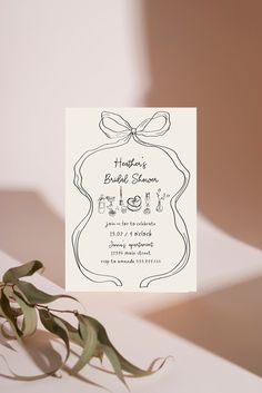 a white card with a bow on it next to some green leaves and a plant