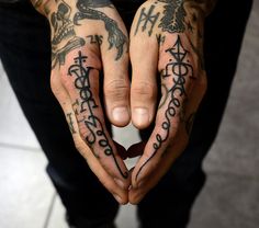 two hands with tattoos on them holding something in the shape of a heart and cross