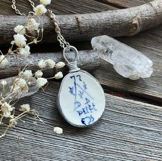 a white and blue pendant with writing on it next to some branches, flowers and rocks