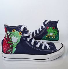 a pair of blue shoes with green and red frogs painted on the upper part of them