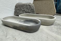 two cement bowls sitting next to each other on top of a stone slab with a rock in the background