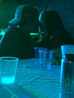 two people are sitting at a table with cups and water in front of their faces