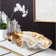 a white vase with flowers in it sitting on a table next to a gold plate