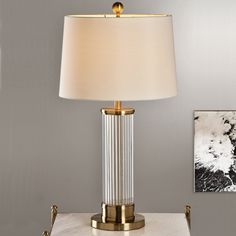 a table lamp with a white shade sitting on top of a marble counter next to a framed photograph