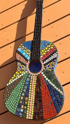 a colorful mosaic guitar sitting on top of a wooden table next to a shadow cast wall