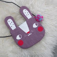 a purple bunny bag with a pink flower in it's mouth on a white furry surface