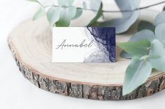 a place card sitting on top of a piece of wood next to some green leaves