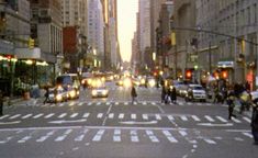 a city street filled with lots of traffic next to tall buildings and people walking on the sidewalk