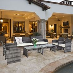 an outdoor living area with wicker furniture and large pool in the background at dusk