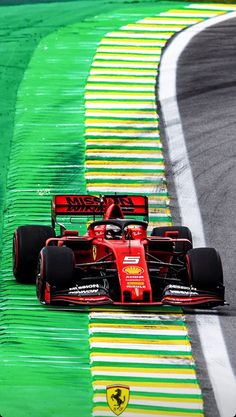 a red race car driving down a track with green and yellow stripes on it's sides