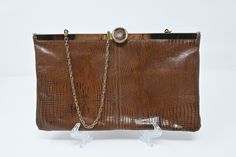 Gorgeous classic brown clutch made out of an alligator leather-like material. It has clasp on the top that flips up to open. The bag itself has a double hinged opening to give you full access to all the little goodies hiding at the bottom of your bag! It is fully lined and ready to be taken out on the town.   Good, vintage condition. Some tarnishing / wear on the back of the gold cap at the top. Measurements: 11 W x  6.5" H x .5" D 18.5" drop at strap Please reach out with any questions prior to Brown Party Clutch With Chain Strap, Elegant Formal Clutch With Crocodile Pattern, Brown Rectangular Clutch With Fold Over Clasp, Vintage Brown Bag With Chain Strap, Evening Clutch With Crocodile Pattern, Brown Crocodile Pattern Evening Shoulder Bag, Elegant Evening Clutch With Crocodile Pattern, Evening Brown Crocodile Pattern Shoulder Bag, Evening Brown Bag With Crocodile Pattern