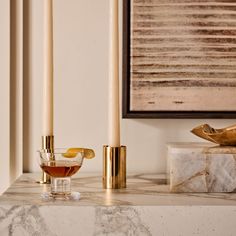 two candles on a marble table next to a vase with a liquid in it and a gold candle holder