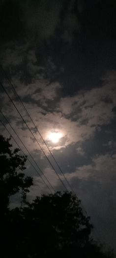 the full moon shines brightly in the dark sky above some power lines and trees