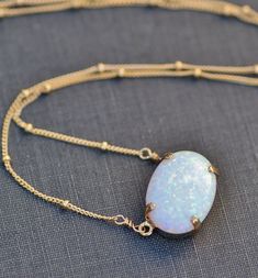 "A stunning necklace made using a lab created opal cabochon. This opal is a lovely shade of white with rainbow fire and flash. The opal is set into a 14K gold filled prong setting and hangs from gold filled satellite style chain. Opal measures 18mm wide (3/4\") or are 14x10mm wide, and is a rounded oval shape. Necklace closes with a gold filled clasp. Please choose desired chain length and opal size at checkout. 18x13mm shown above. Also available in rose gold and silver. Silver will have silver Opal Gifts, Opal Pendant Necklace, White Rainbow, October Birthstone, Chain Gold, Stunning Necklace, Opal Pendants, Opal Necklace, October Birth Stone